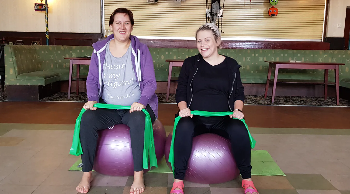 Two pregnant Start Right Pilates members using resistance bands while seated on stability balls